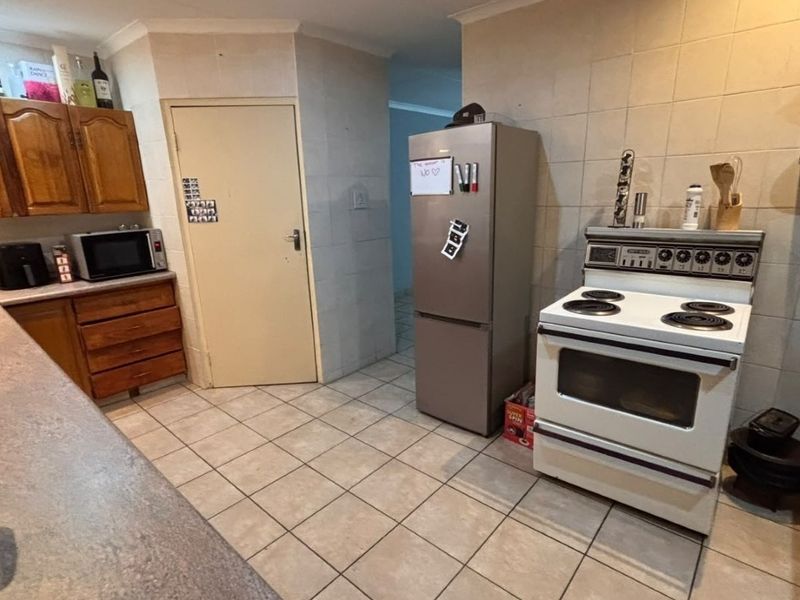 A functional kitchen featuring wooden cabinetry, tiled walls and flooring, and a freestanding stove, offering a practical layout with potential for modern updates.