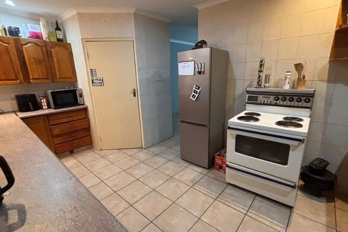 A functional kitchen featuring wooden cabinetry, tiled walls and flooring, and a freestanding stove, offering a practical layout with potential for modern updates.