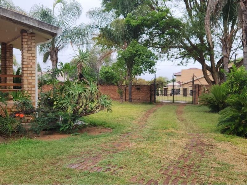 A view of the front garden featuring a brick boundary wall, metal driveway gate, and a covered patio area with brick pillars.