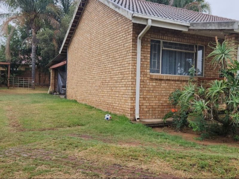 A side view of a face brick house featuring a tiled roof, gutters, and aluminium window frames set within a garden area.