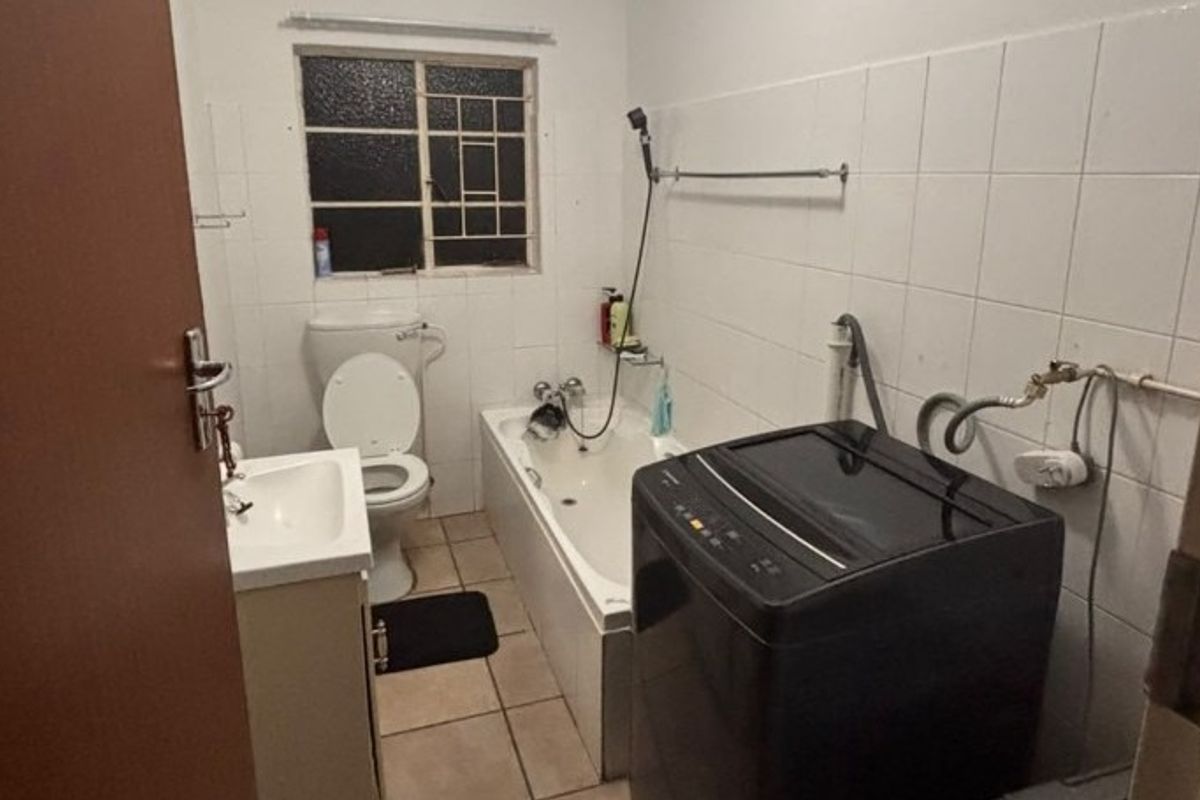 A functional bathroom featuring a bathtub, toilet, and vanity basin, with tiled finishes and integrated laundry plumbing connections.