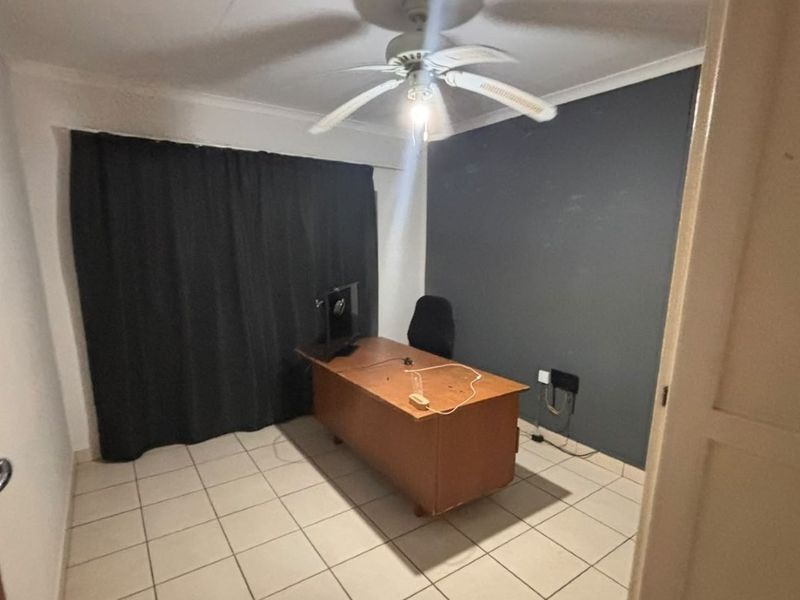 A functional office space featuring tiled flooring, a ceiling fan, and a dark accent wall, providing a versatile area for work or study.