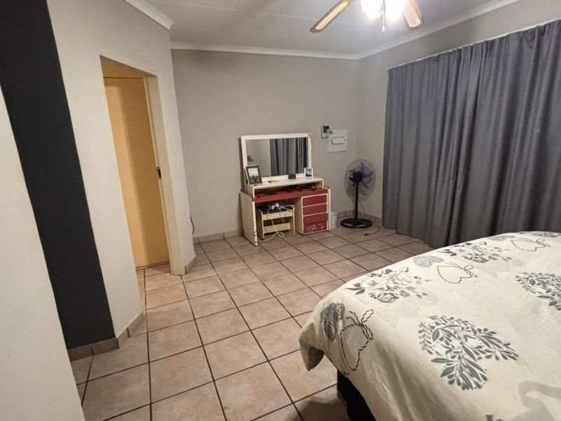 A spacious bedroom featuring neutral wall tones, tiled flooring, and a ceiling fan, offering a functional layout with ample natural light potential.