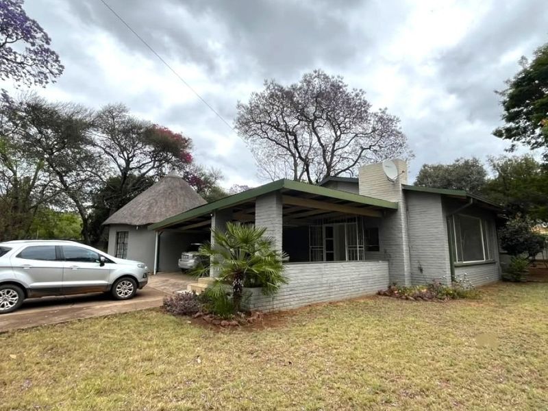 Front view of a single-story house featuring a painted brick facade, a covered patio area, and a distinctive thatched roof section.