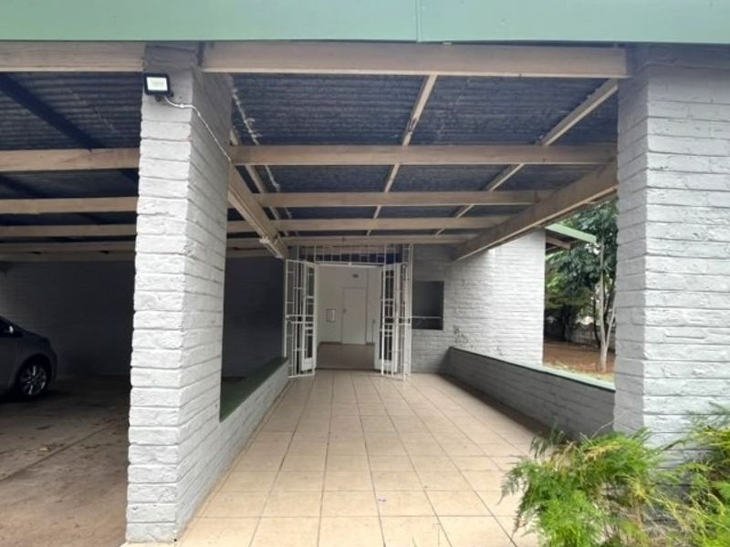 A covered front entrance and carport area featuring brick pillars, tiled flooring, and a secure gated entry point.