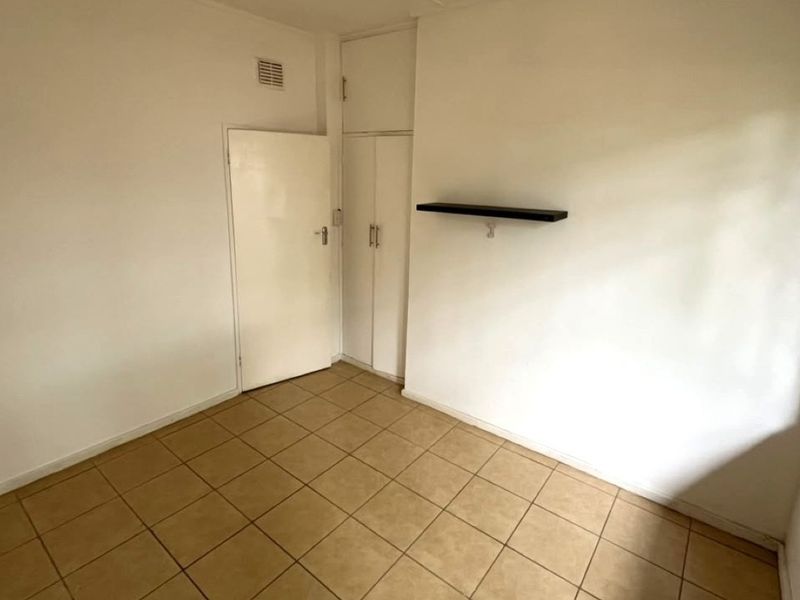An empty bedroom featuring tiled flooring and a built-in cupboard, providing a blank canvas for personalization.
