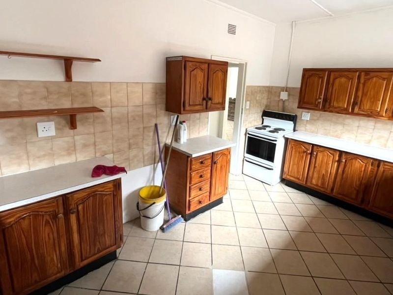 A functional kitchen featuring wooden cabinetry, tiled backsplash, and tiled flooring, equipped with a freestanding stove and ample counter space.