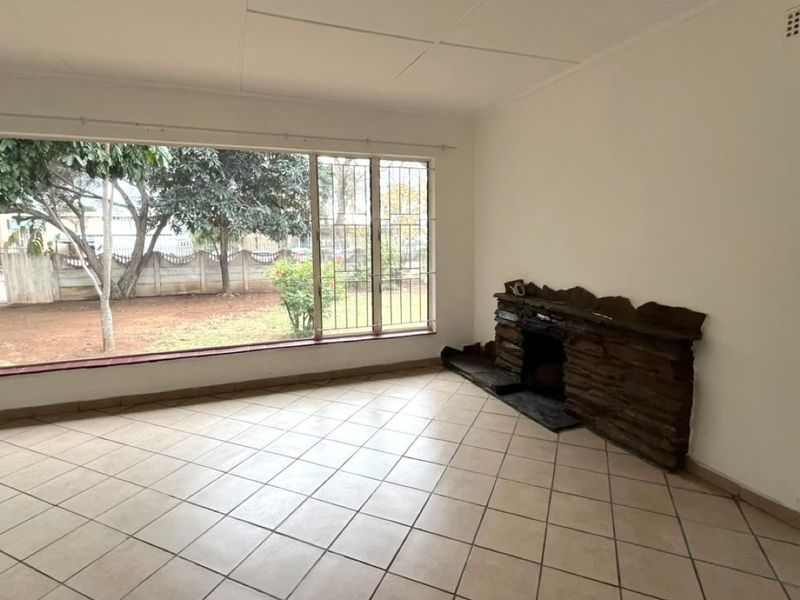 Spacious living room featuring tiled flooring, a large picture window with security bars, and a rustic stone fireplace.