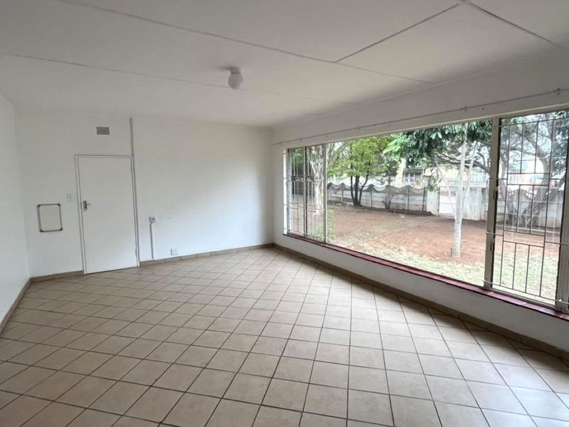 A spacious, empty living room featuring large windows with security bars, tiled flooring, and neutral walls, offering a bright and versatile living space.