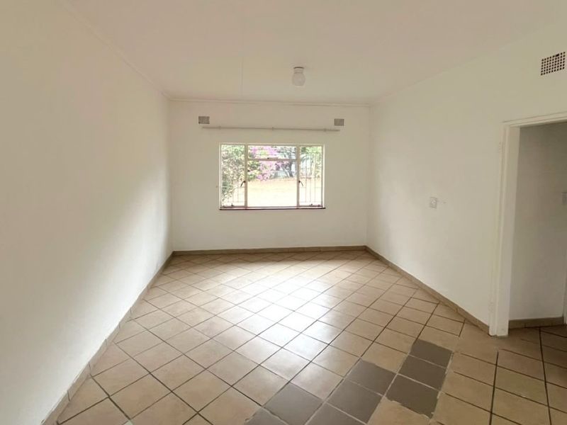 An empty living room featuring tiled flooring, a window with security bars, and neutral walls, ready for personalization.