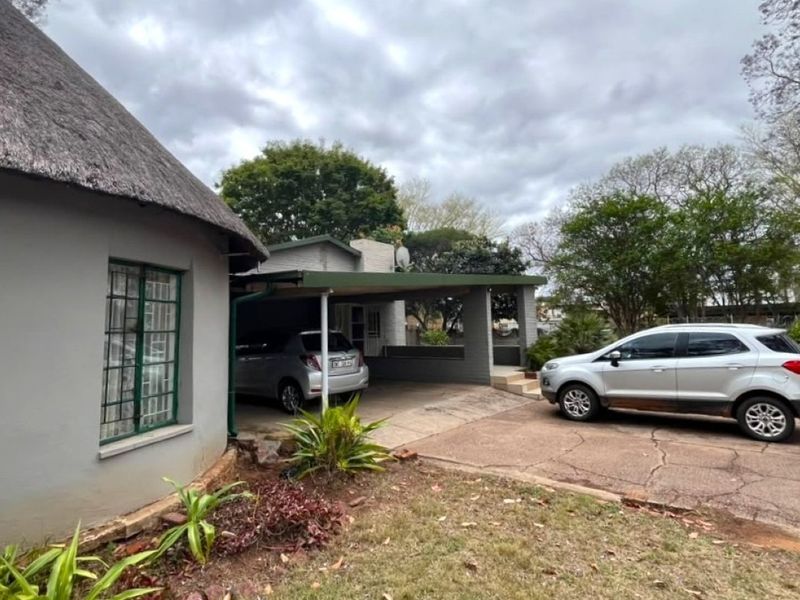Front exterior view of the property featuring a thatched roof section, a covered carport, and a paved driveway.