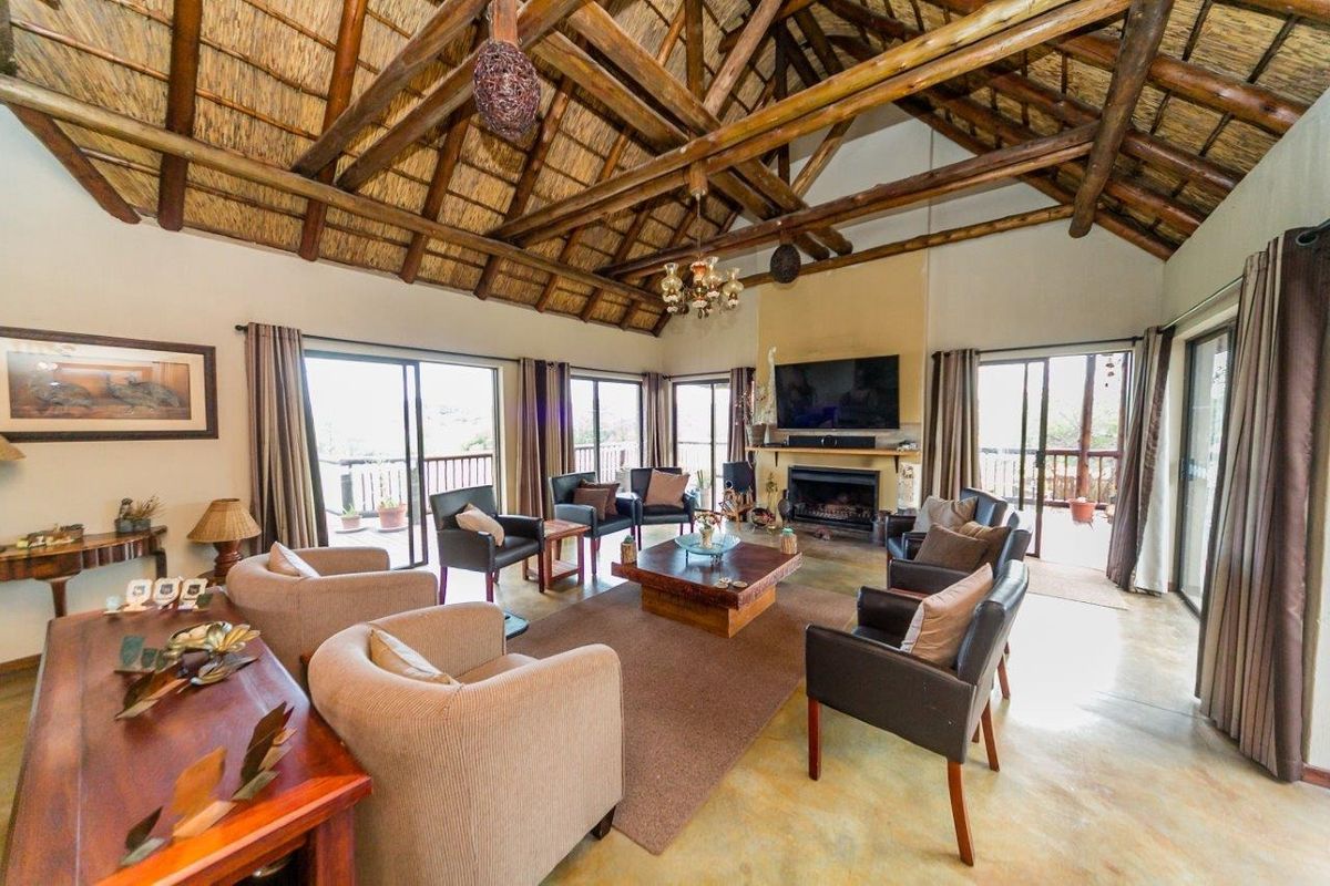 Spacious living room featuring a high vaulted thatched ceiling with exposed timber beams, a built-in fireplace, and large sliding glass doors leading to the patio.