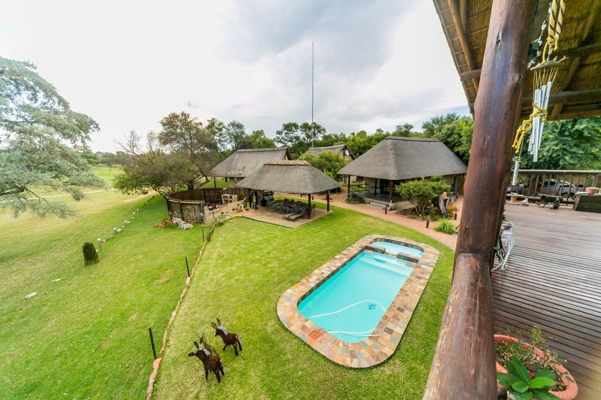 Elevated view of a guest house property featuring a swimming pool, thatched-roof structures, a wooden deck, and expansive landscaped garden grounds.