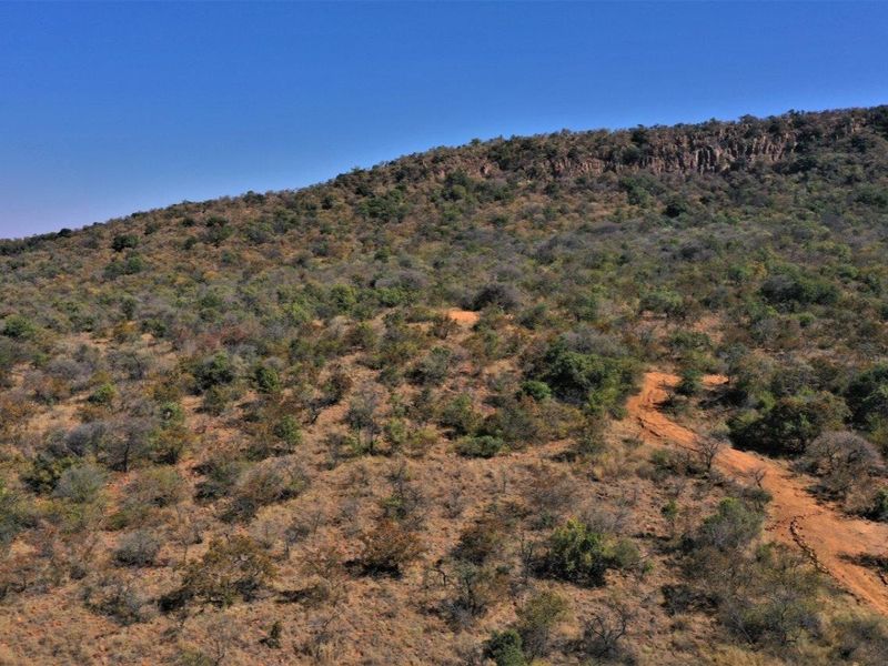 An aerial view of a vacant residential plot featuring natural bushveld vegetation, rolling terrain, and a dirt access track.