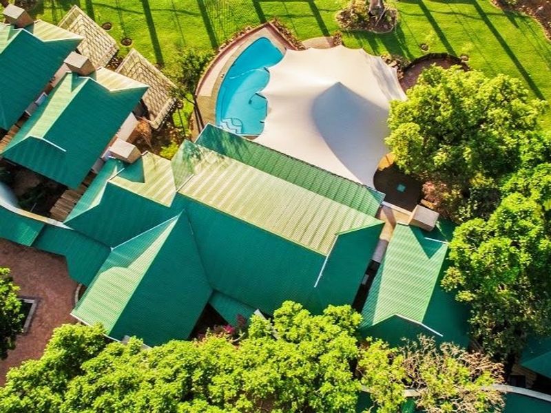 Aerial view of the farm property showcasing the green metal roof structure, swimming pool with shade sail, and surrounding landscaped garden areas.