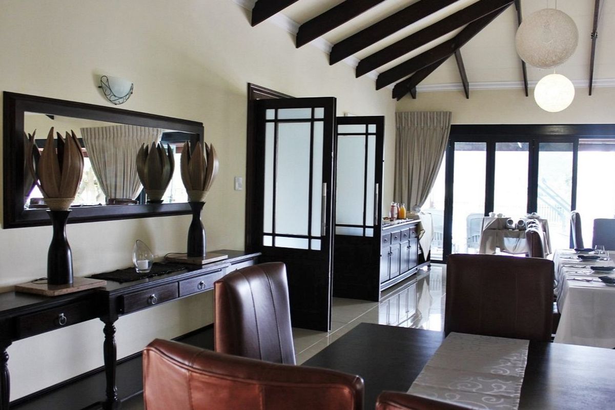 Spacious living area featuring vaulted ceilings with exposed timber beams, tiled flooring, and double glass-paneled doors leading to an outdoor patio.