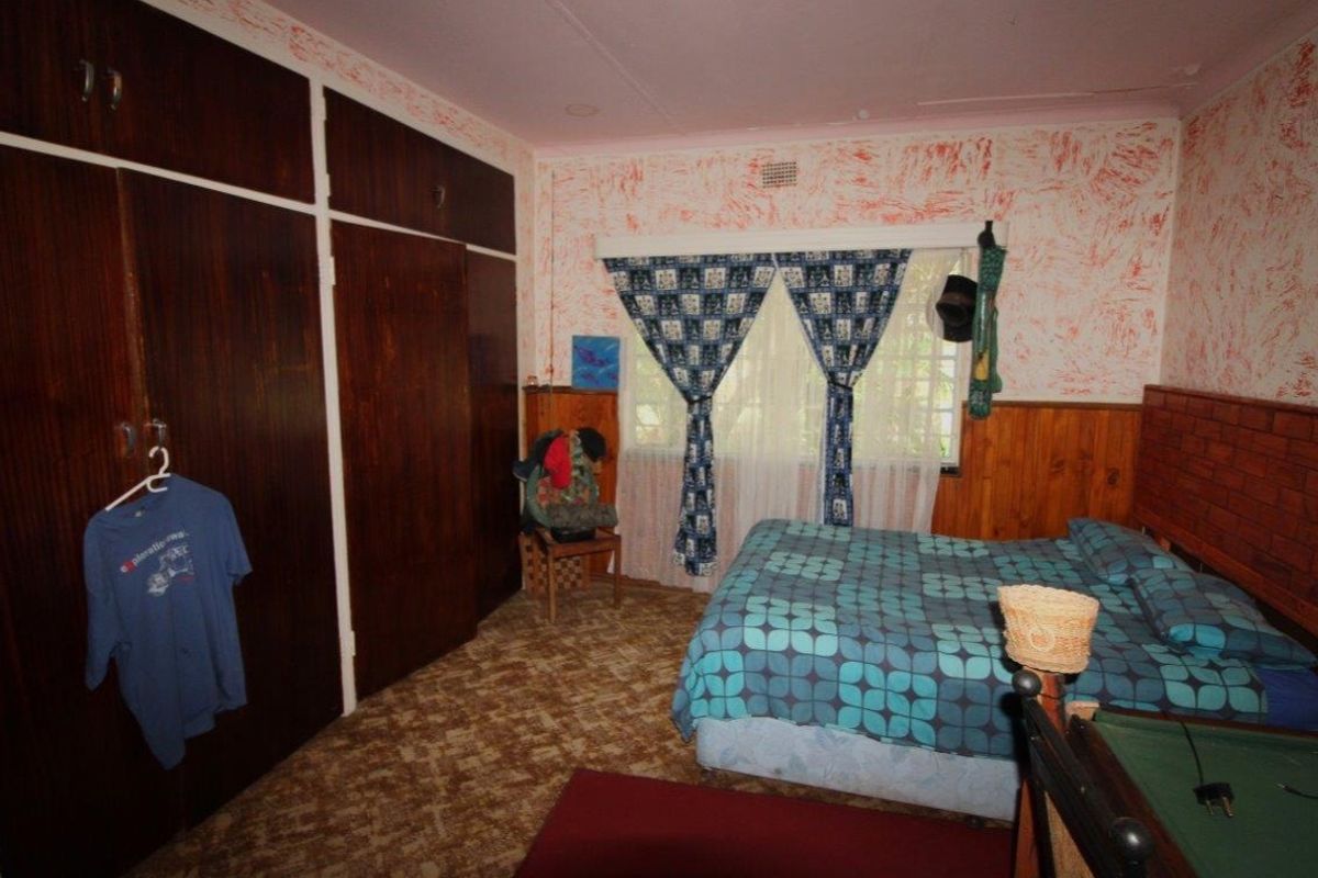 A bedroom featuring built-in wooden cupboards, wood paneling, and patterned wall finishes, offering a dated aesthetic ready for modernization.