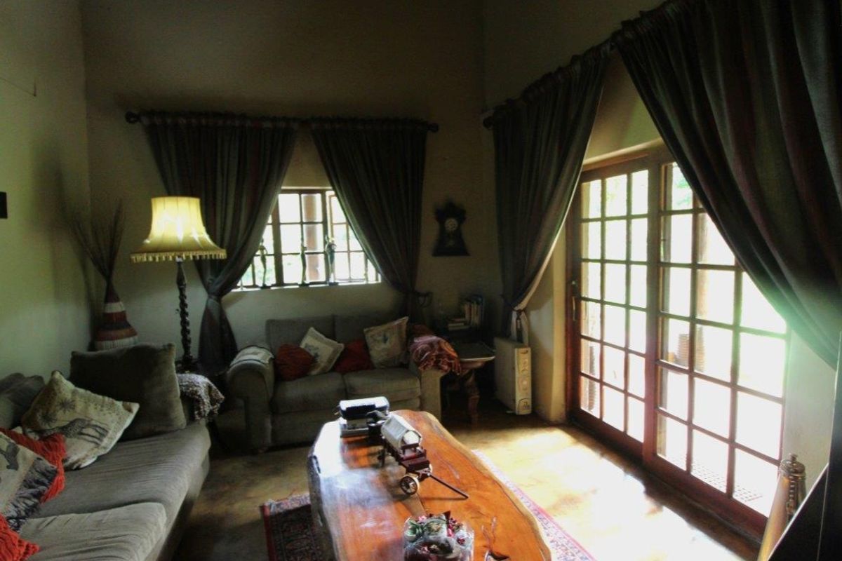 A cozy living room featuring high ceilings, tiled flooring, and large wooden-framed glass doors providing natural light and access to the outdoors.