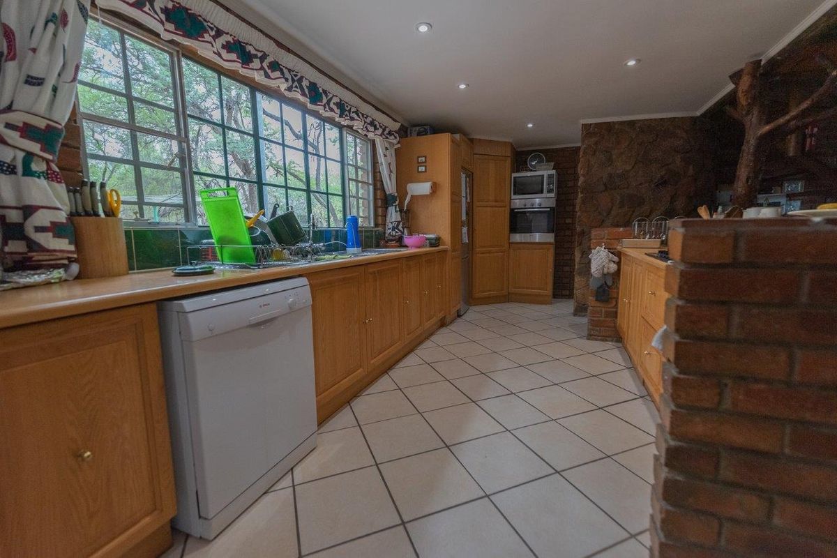 A rustic kitchen featuring wooden cabinetry, tiled flooring, built-in oven, and large windows overlooking the garden.