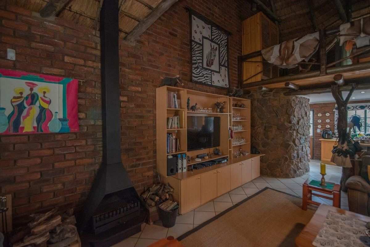 Rustic living area featuring exposed brick walls, a high thatched ceiling, a built-in fireplace, and a stone-clad feature wall with a mezzanine level.
