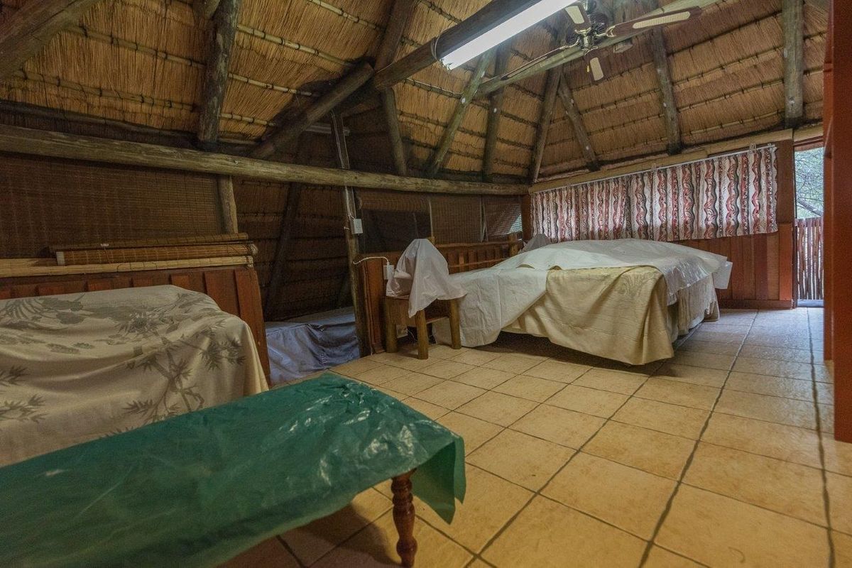 Rustic bedroom featuring a high vaulted thatch ceiling with exposed timber beams and tiled flooring.