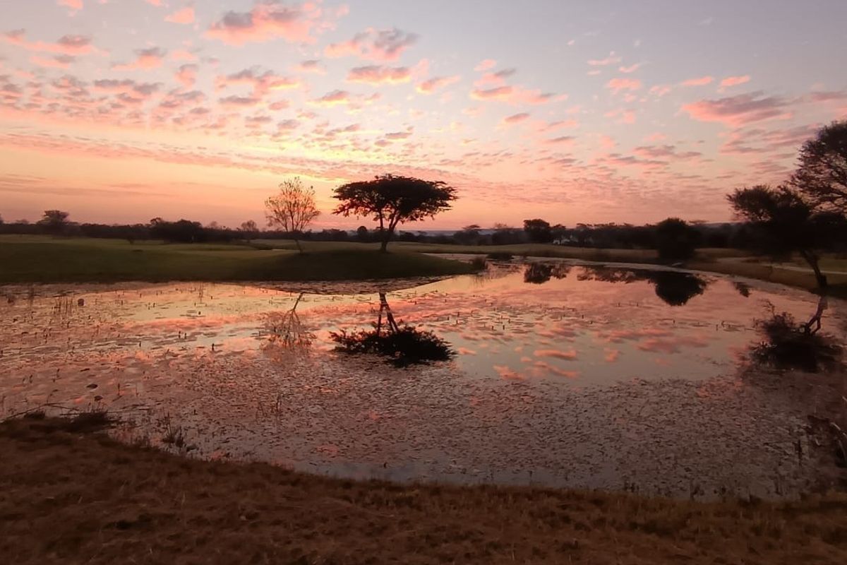 A scenic view of a natural pond and landscaped grounds at sunset, showcasing the tranquil outdoor environment of the residential land.