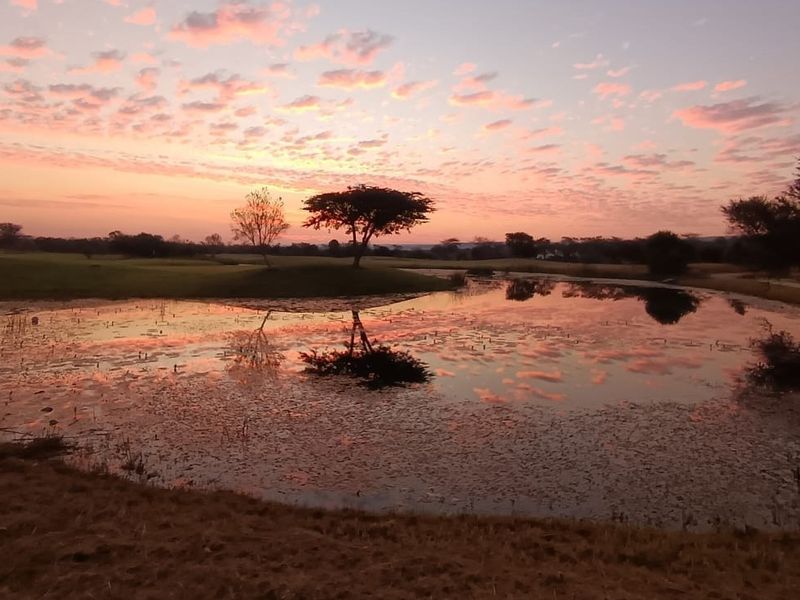 A scenic view of a natural pond and landscaped grounds at sunset, showcasing the tranquil outdoor environment of the residential land.