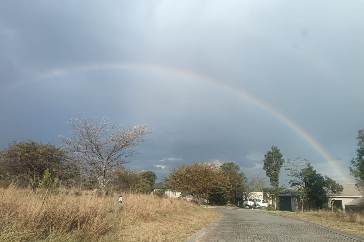 A view of the paved residential street and surrounding landscape under a rainbow, showcasing the neighborhood approach and access.