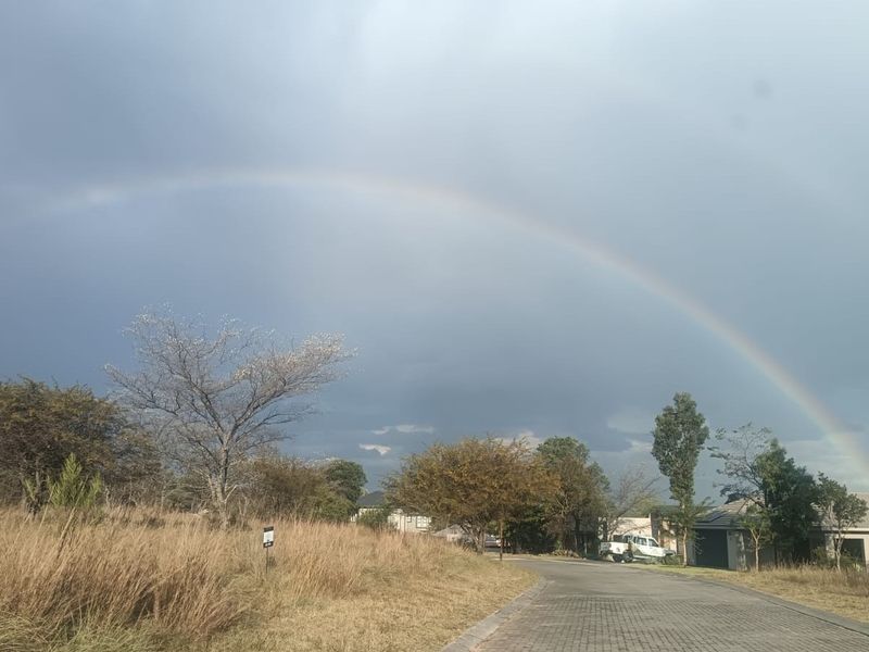 A view of the paved residential street and surrounding landscape under a rainbow, showcasing the neighborhood approach and access.