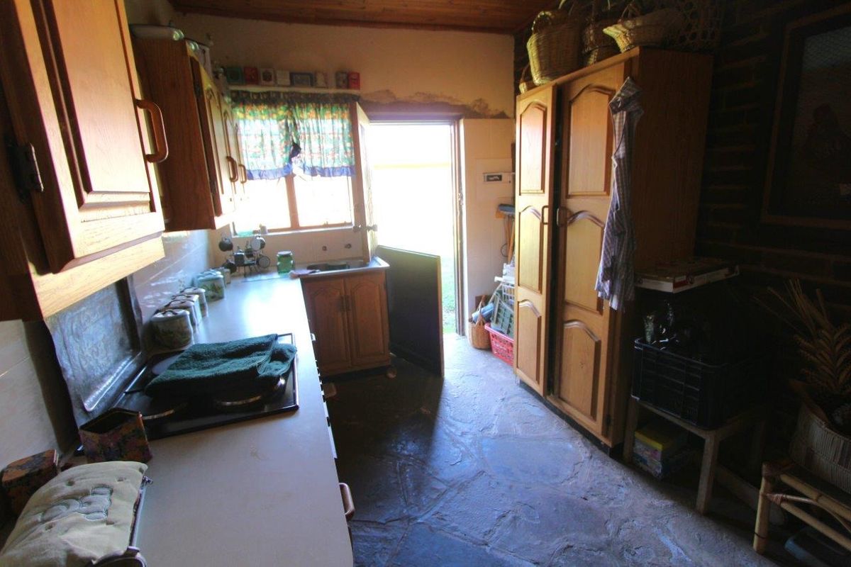 A rustic kitchen featuring wooden cabinetry, stone flooring, and direct access to the exterior, offering a traditional farm-style aesthetic.