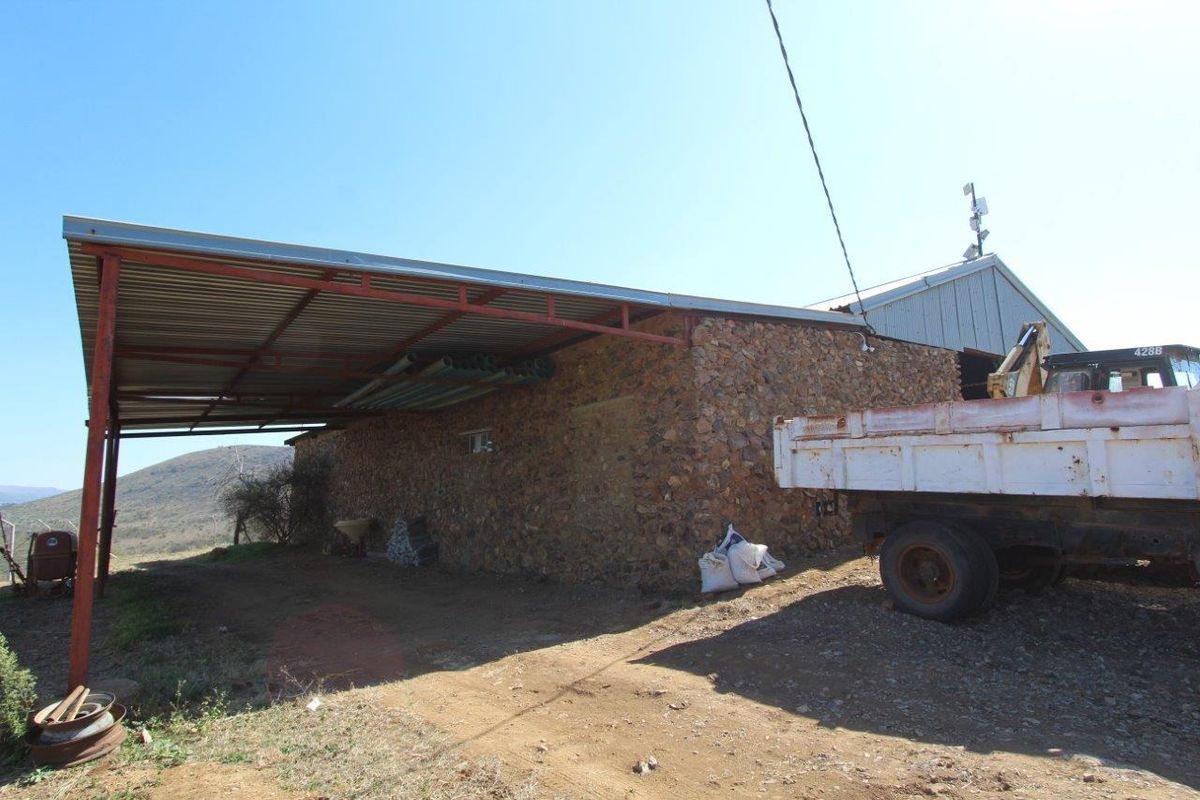 A rustic farm outbuilding featuring stone masonry walls and a large covered metal-roofed lean-to area, suitable for storage or agricultural utility purposes.