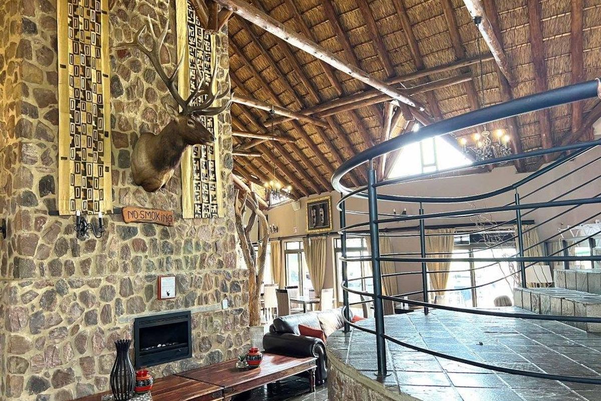 Spacious living area featuring a high vaulted thatched ceiling, exposed timber beams, and a prominent stone-clad fireplace with a built-in hearth.