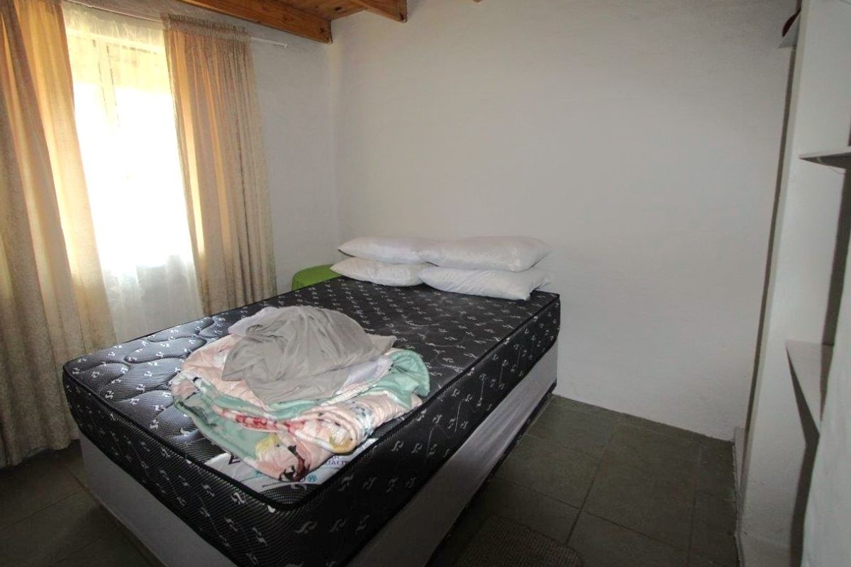 A simple bedroom featuring tiled flooring, exposed timber ceiling beams, and natural light from a window.
