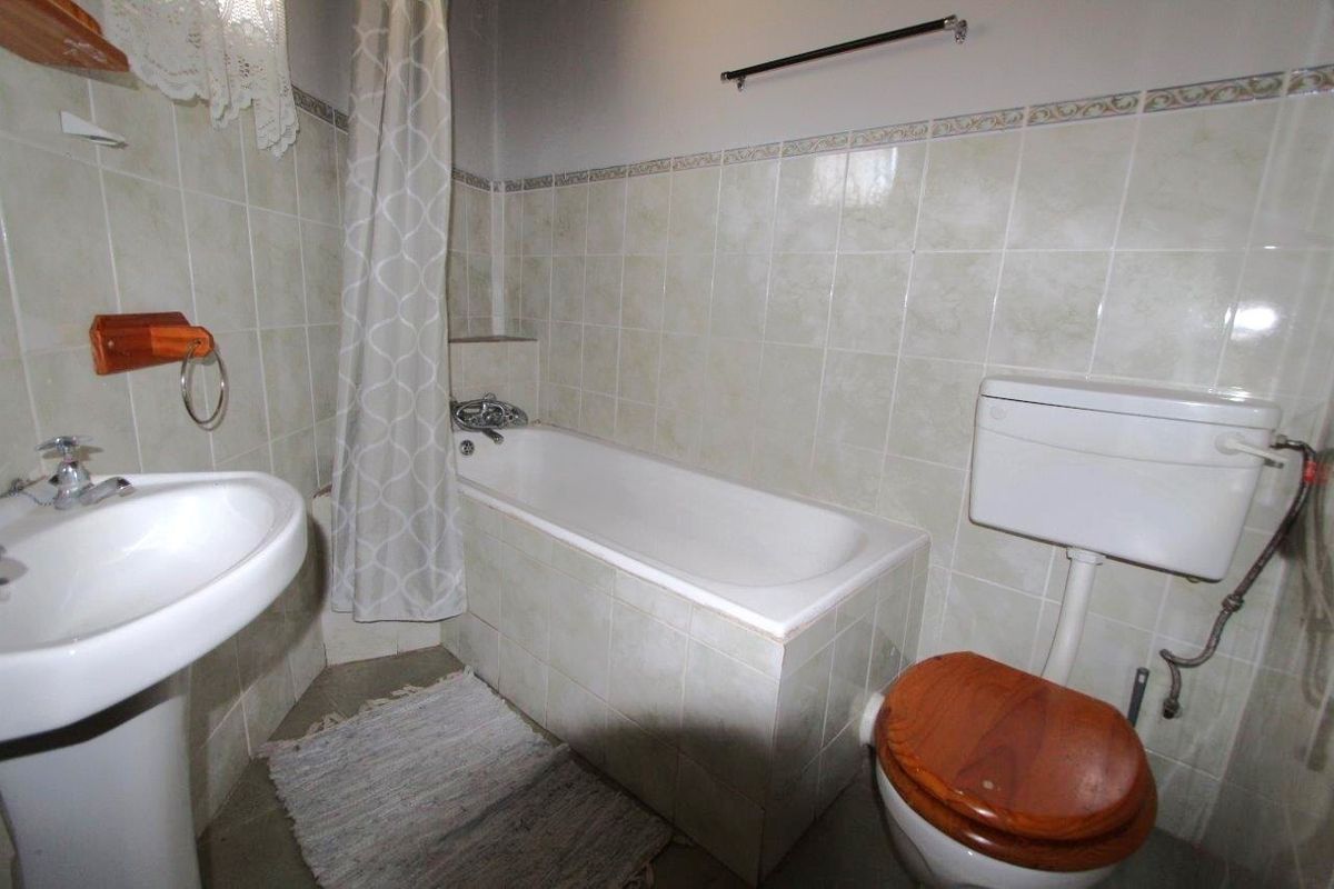 A dated bathroom featuring a standard bathtub with shower attachment, pedestal basin, and toilet, finished with neutral wall tiling.