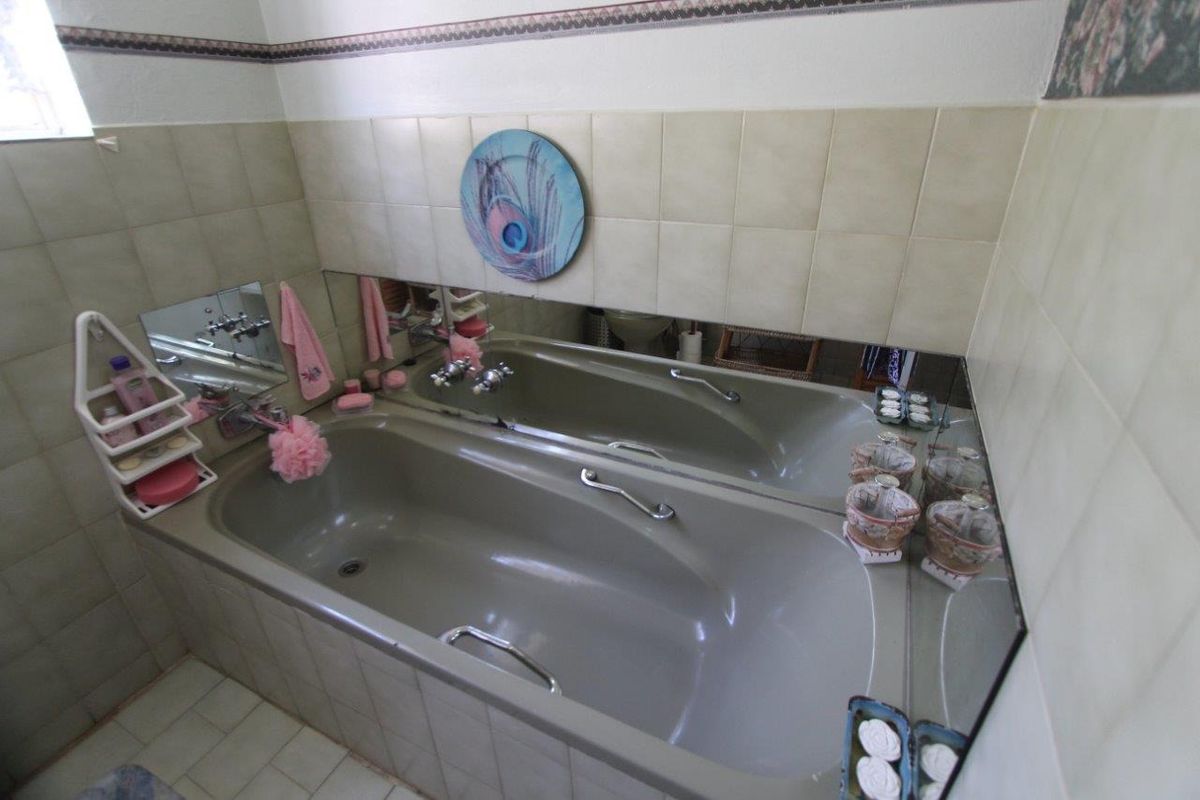 A dated bathroom featuring a built-in bathtub with integrated grab rails, tiled surround, and a large wall-mounted mirror.