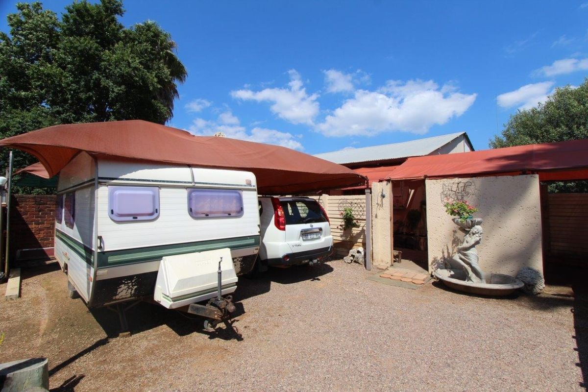 Outdoor area featuring a gravel driveway, shade cloth carport structure, and a decorative water feature against a masonry wall.
