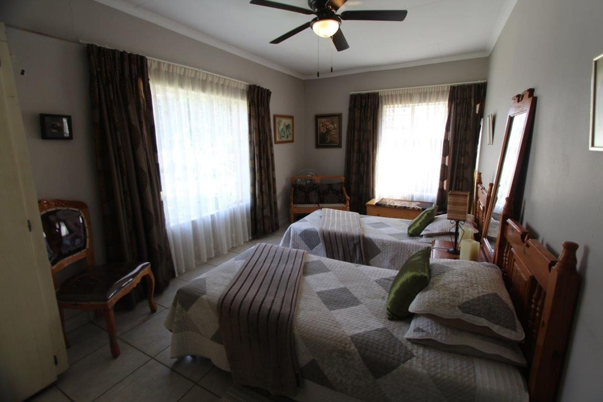 A bedroom featuring tiled flooring, a ceiling fan, and dual windows with curtains, providing a functional and well-lit sleeping space.