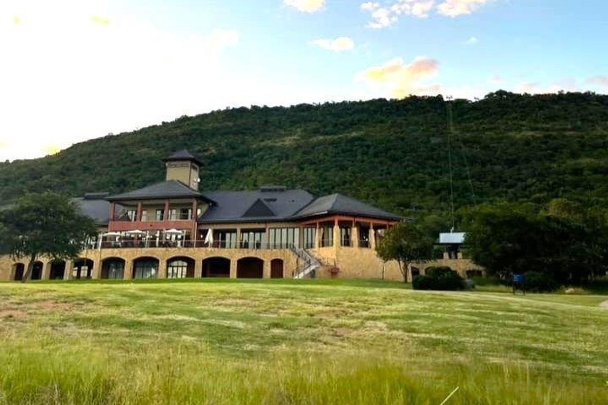 A view of the rear elevation of a large residential property featuring stone cladding, a covered patio, and a balcony set against a mountain backdrop.