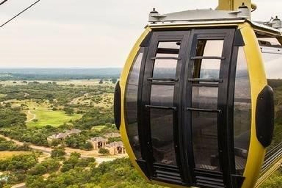 An aerial view featuring a cable car cabin overlooking a scenic landscape with residential properties and natural vegetation.