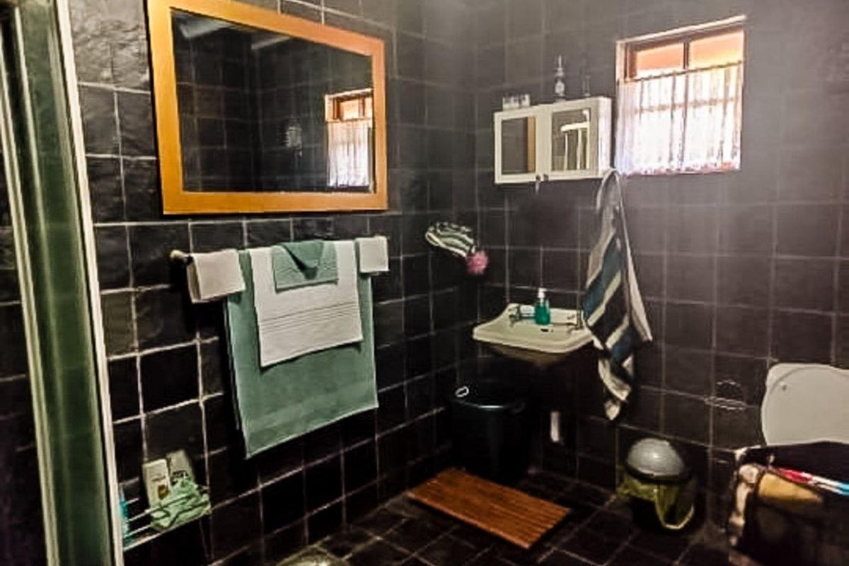 A dated bathroom featuring dark wall and floor tiles, a wall-mounted basin, and a shower enclosure.
