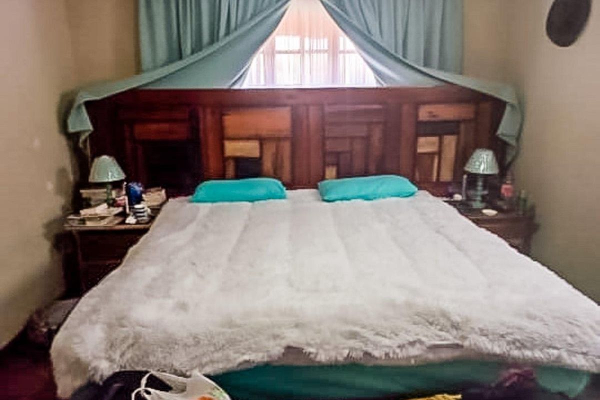 A bedroom featuring a large wooden headboard and window with curtains.