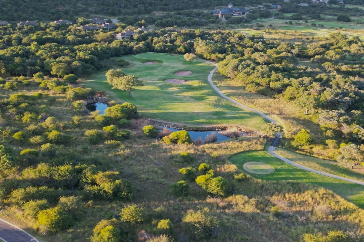 An aerial view of a residential golf estate featuring a well-maintained fairway, natural landscaping, and surrounding indigenous bushveld.