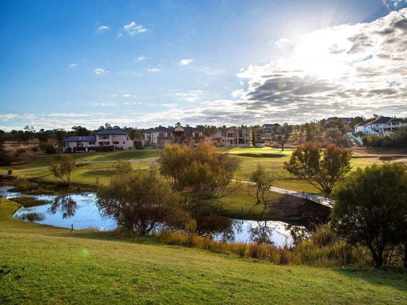 A scenic view of the residential estate landscape featuring manicured green spaces, a tranquil pond, and surrounding luxury homes.
