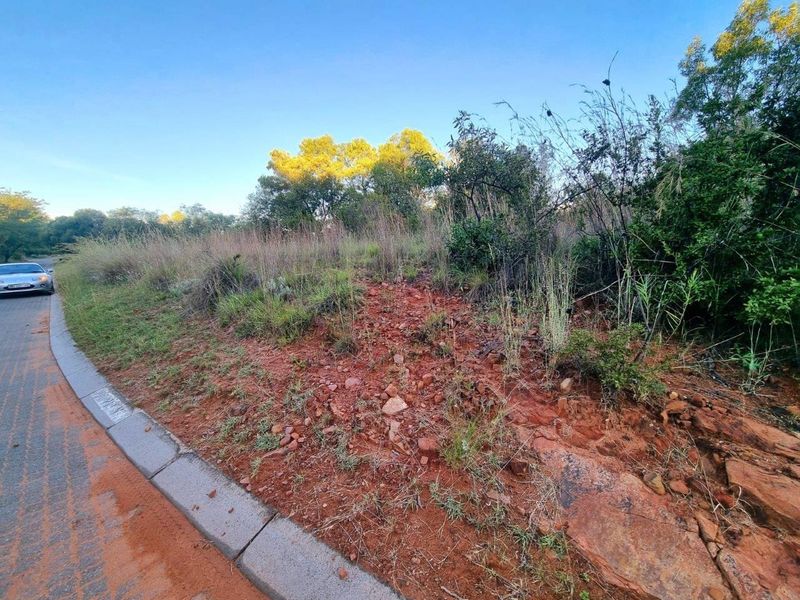 A view of the vacant residential land from the street, featuring natural terrain, native vegetation, and established roadside curbing.