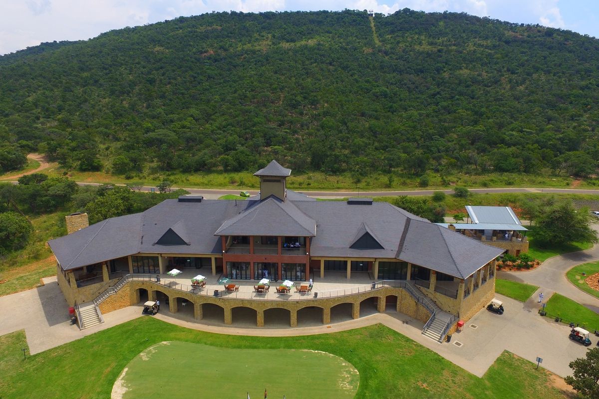 Aerial view of a large clubhouse facility featuring stone architecture, expansive covered patios, and direct access to a golf course in a scenic setting.