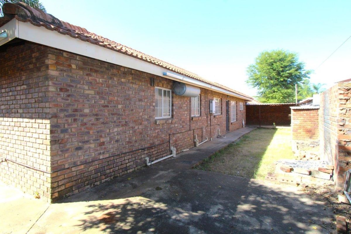 A view of the rear exterior of the house, featuring face-brick walls, a tiled roof, and a concrete pathway leading to a backyard area.