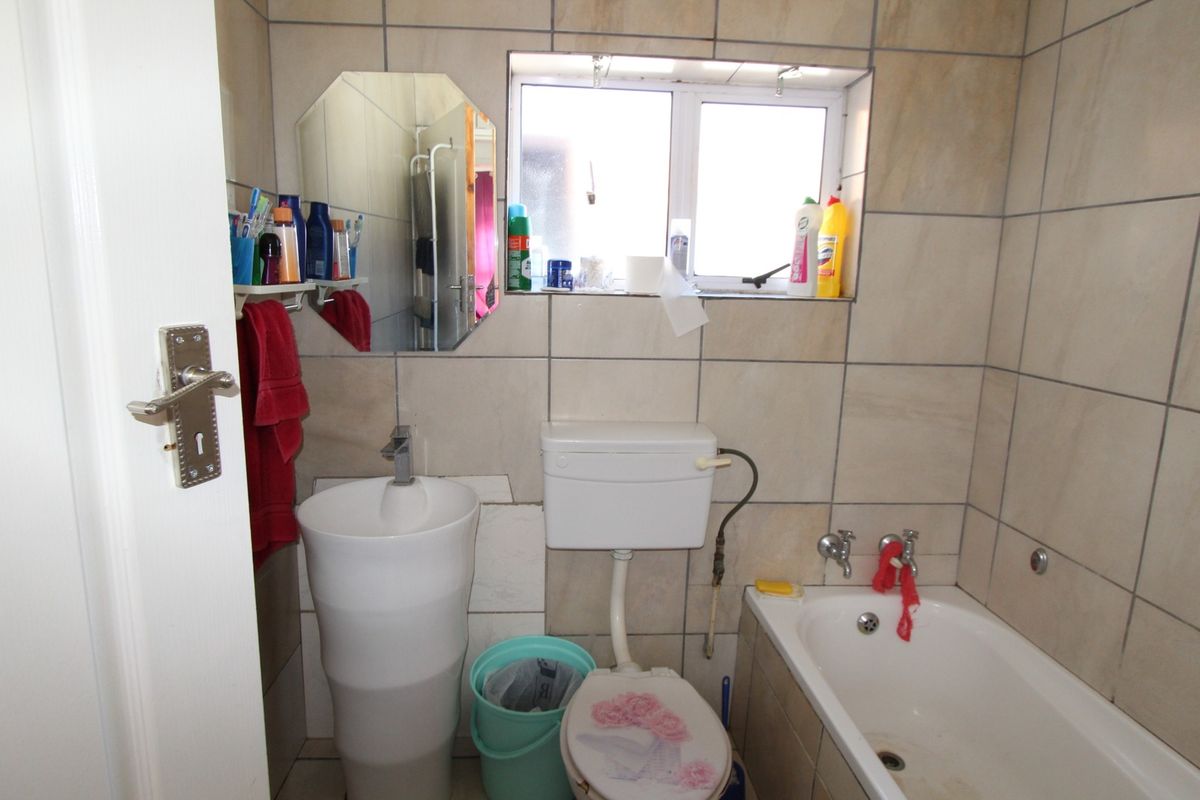 Compact bathroom featuring a pedestal basin, standard toilet, and a built-in bathtub with tiled walls and a small window for natural light.