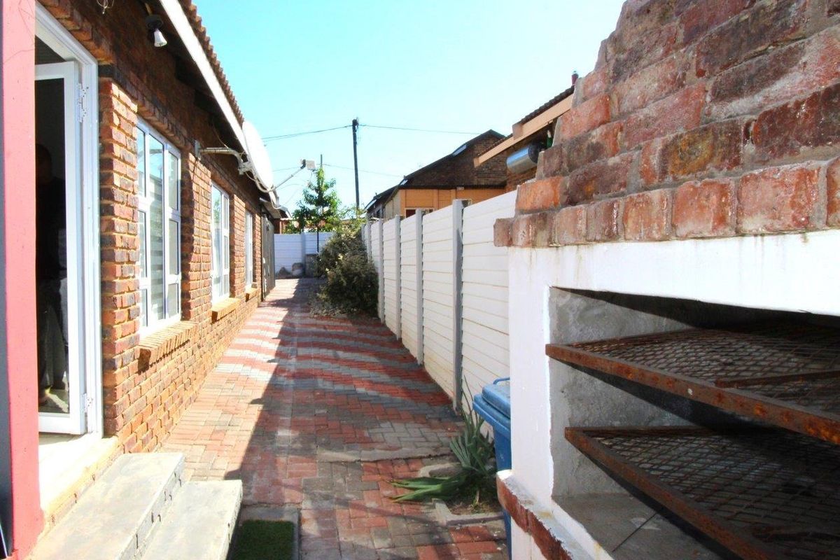 Side exterior area featuring a built-in brick braai, paved walkway, and perimeter walling along the side of the house.
