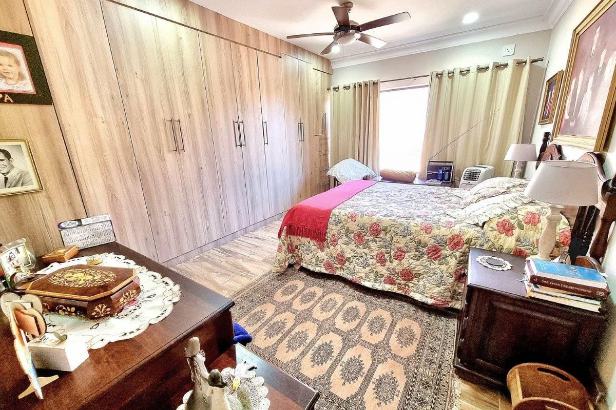 A well-maintained bedroom featuring extensive floor-to-ceiling built-in wooden cabinetry, a ceiling fan, and wood-look flooring.