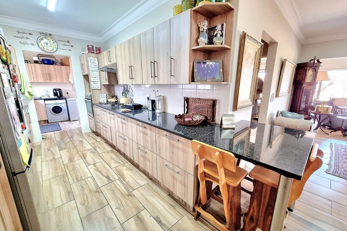 A well-maintained kitchen featuring light wood cabinetry, dark granite countertops, a breakfast bar, and an adjacent scullery area with laundry facilities.